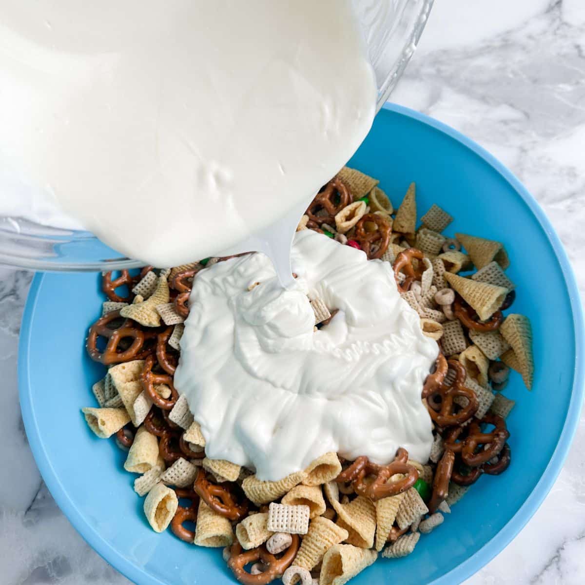 Bowl with snack mix and melted white chocolate being poured on it.