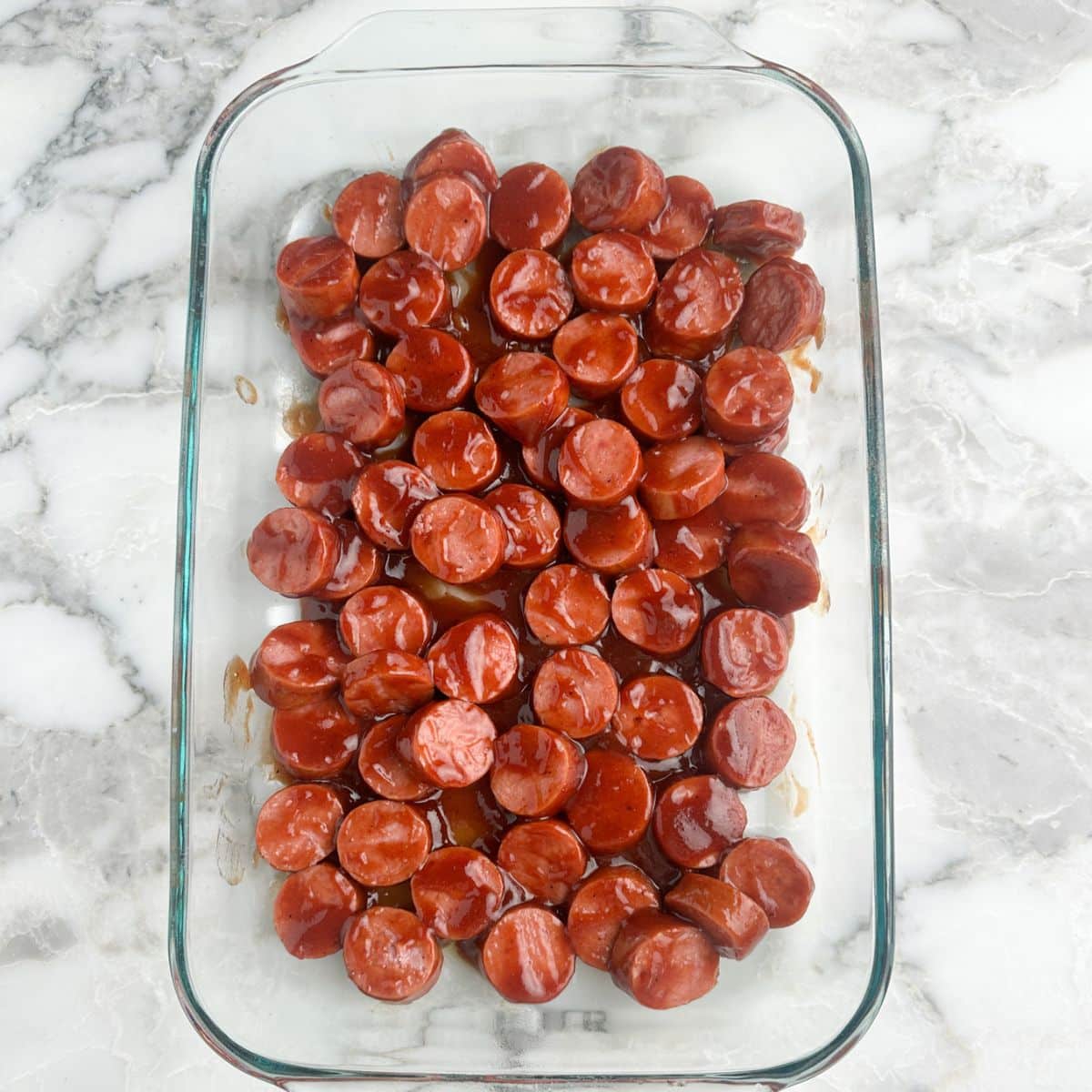 Sliced kielbasa with bbq sauce in a baking dish.