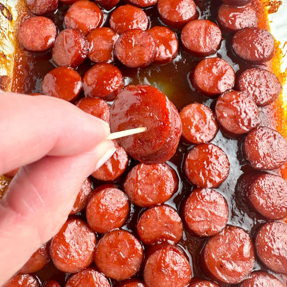 Hand holding sliced sausage on a toothpick.