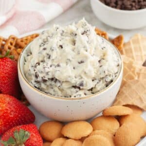 Bowl of chocolate chip cheesecake dip surrounded by cookies and strawberries.