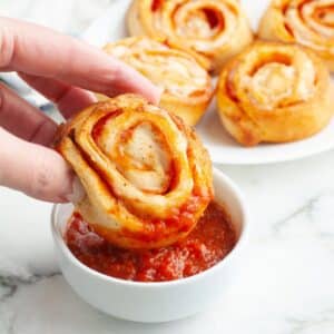 Pepperoni pinwheel dipping into pizza sauce.