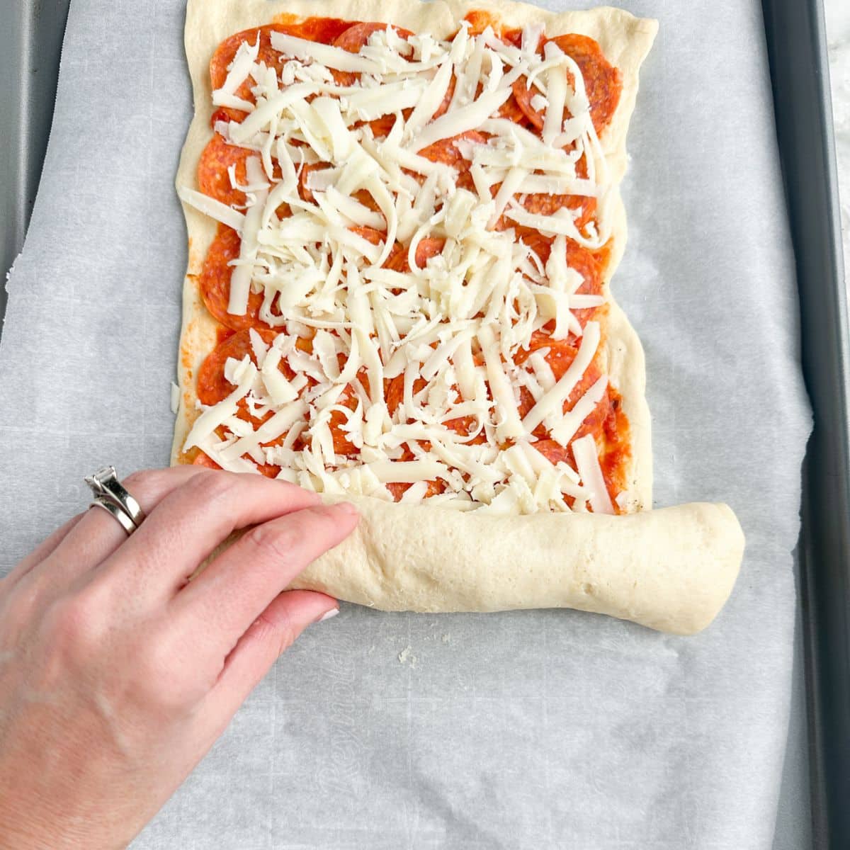 Hand rolling dough with pizza sauce and cheese. 