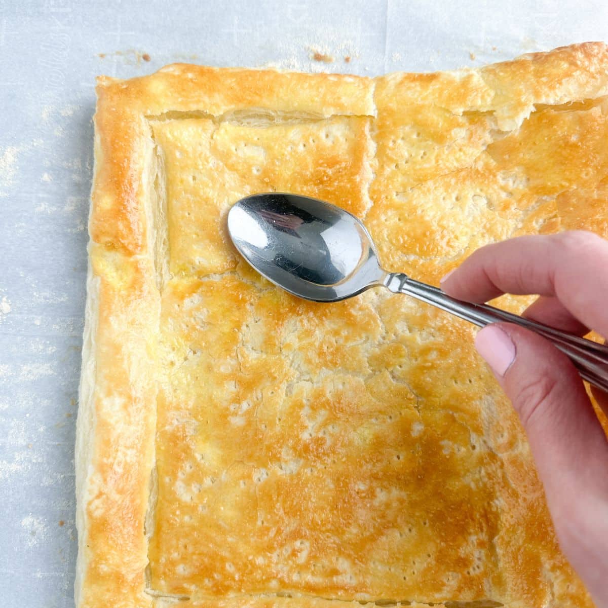 Spoon pushing down baked puff pastry.