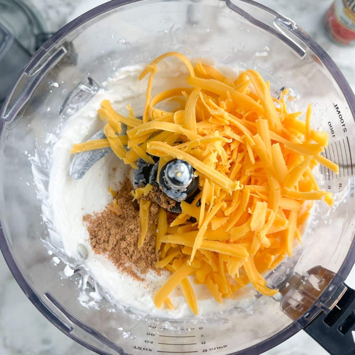 Food processor with shredded cheese, seasoning, and whipped cottage cheese.