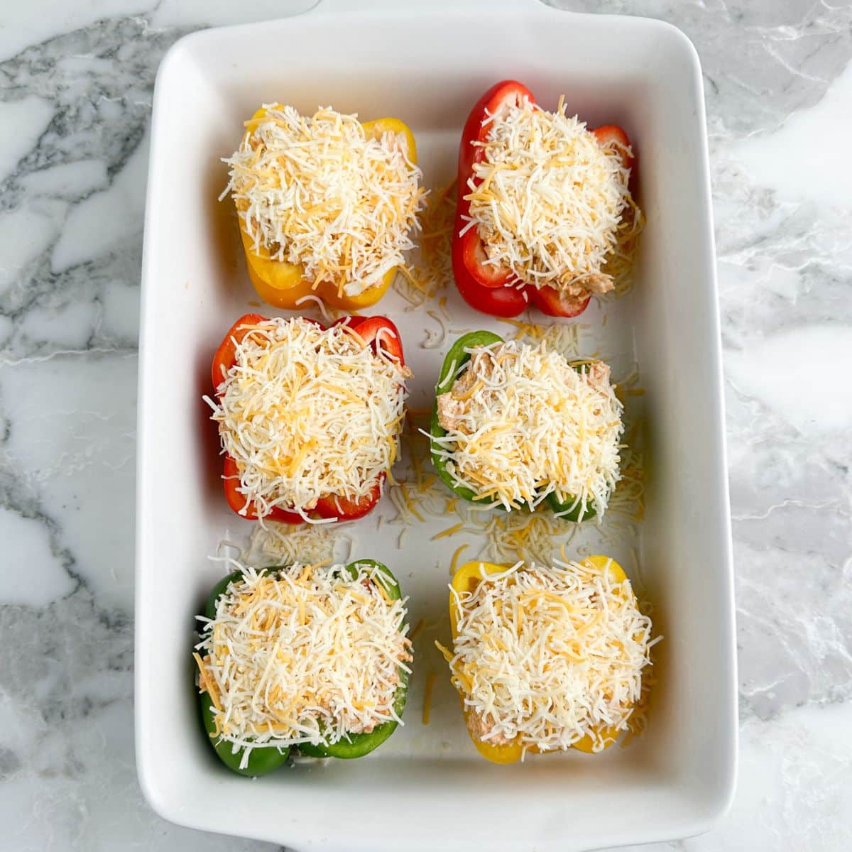 Stuffed pepper with chicken and shredded cheese in a casserole dish.