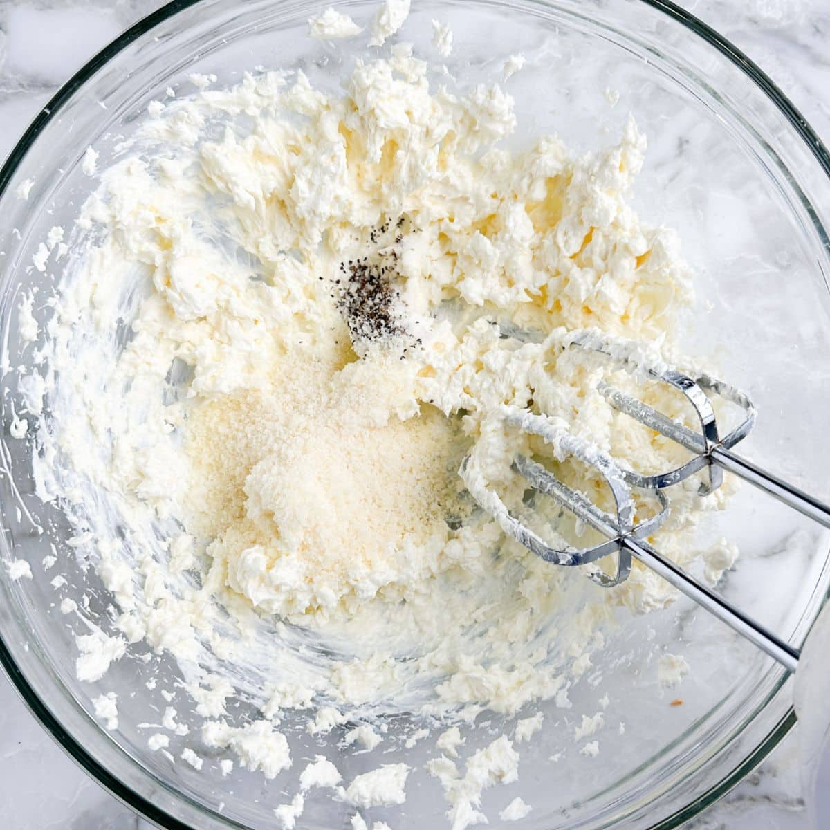 Bowl of cream cheese and parmesan cheese with a mixer. 