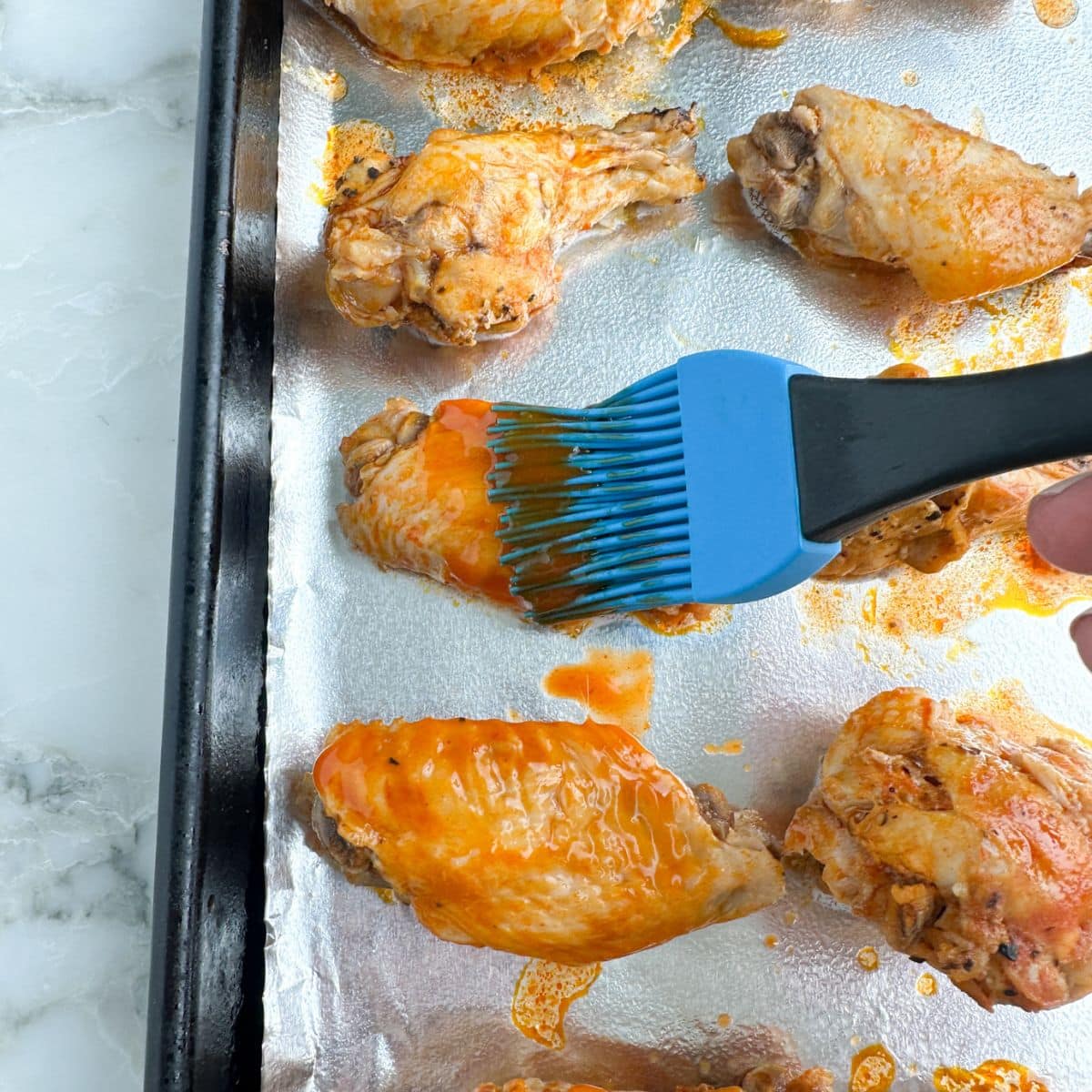 Brushing buffalo sauce on chicken wings. 