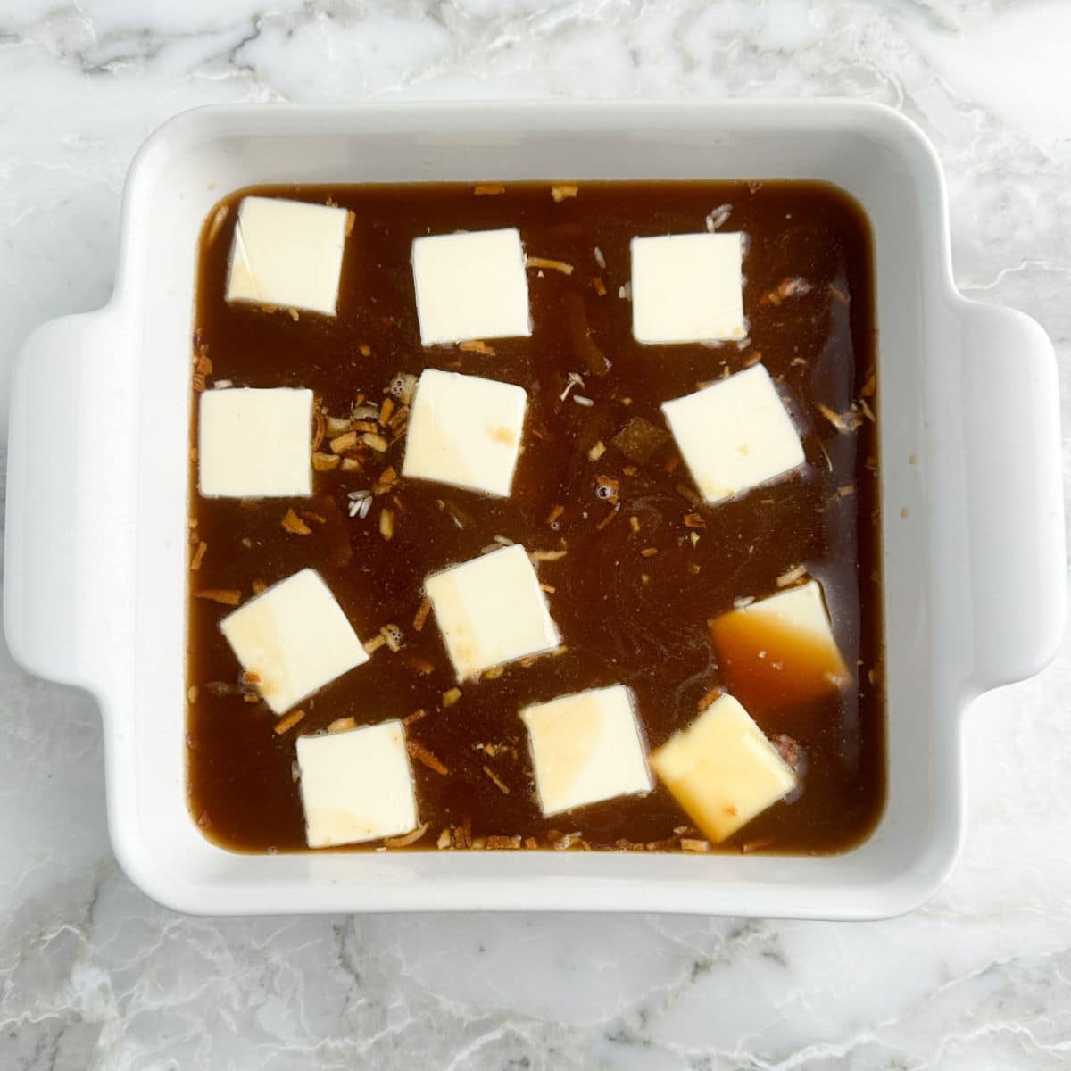 Baking dish with beef broth and pats of butter. 