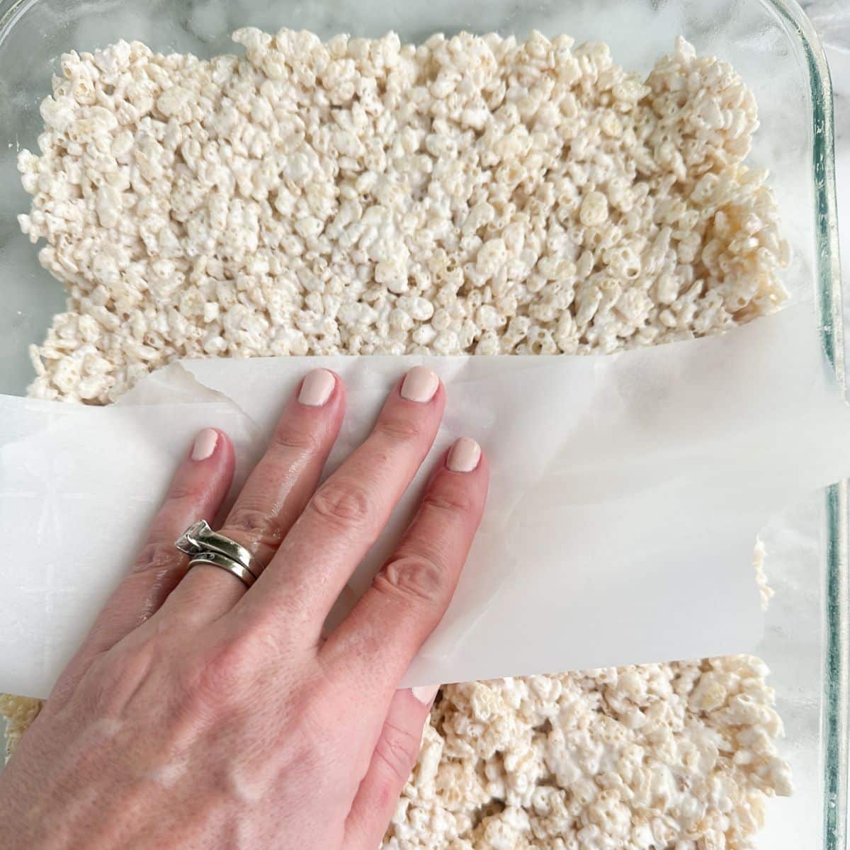 Hand pushing down rice krispie treats into a dish.