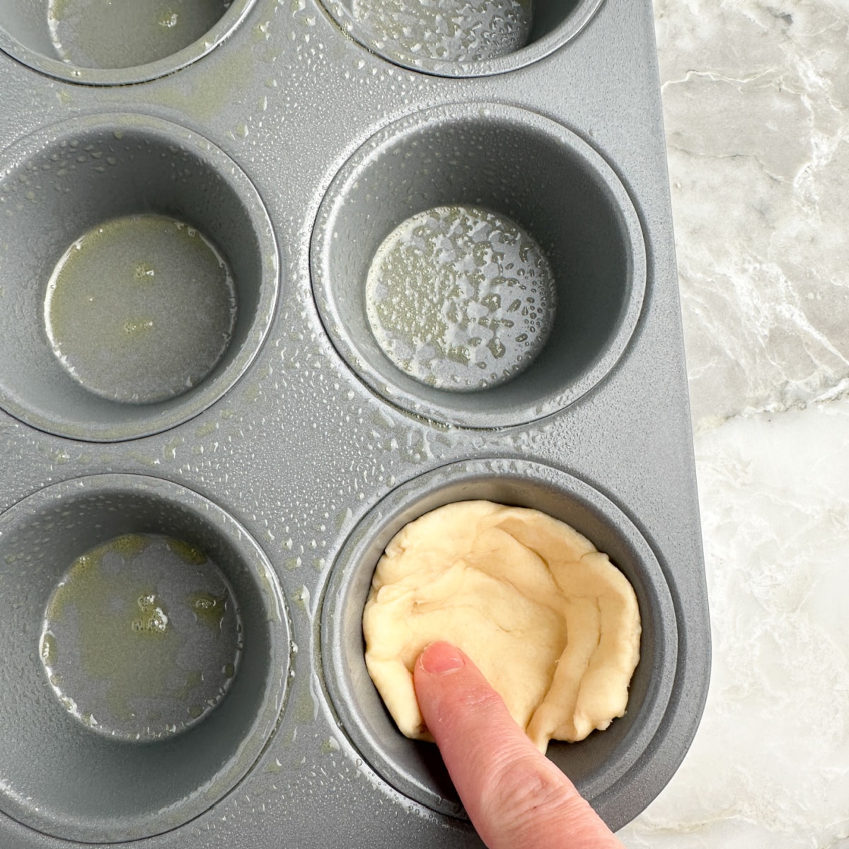 Muffin tip with dough being pressed in the cup. 