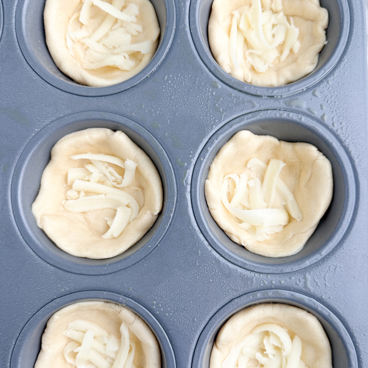 Muffin tin with dough and shredded cheese. 