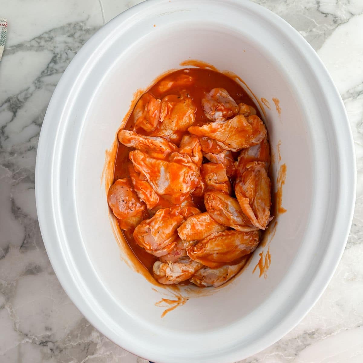 Slow cooker with uncooked buffalo wings. 