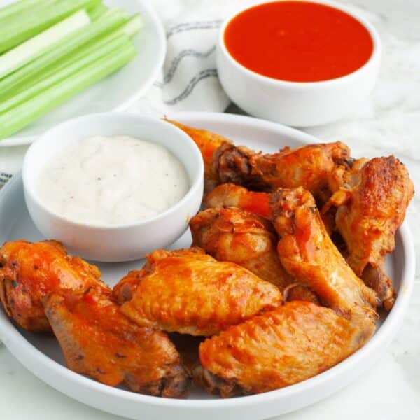 Plate of chicken wings with ranch, celery sticks, and buffalo sauce.