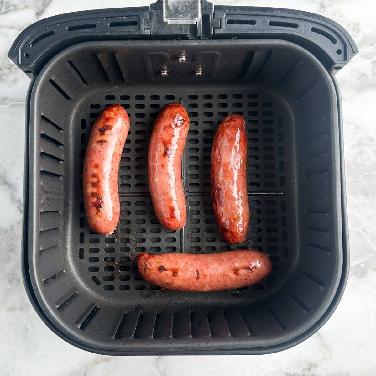 Cooked chicken sausages in air fryer basket. 