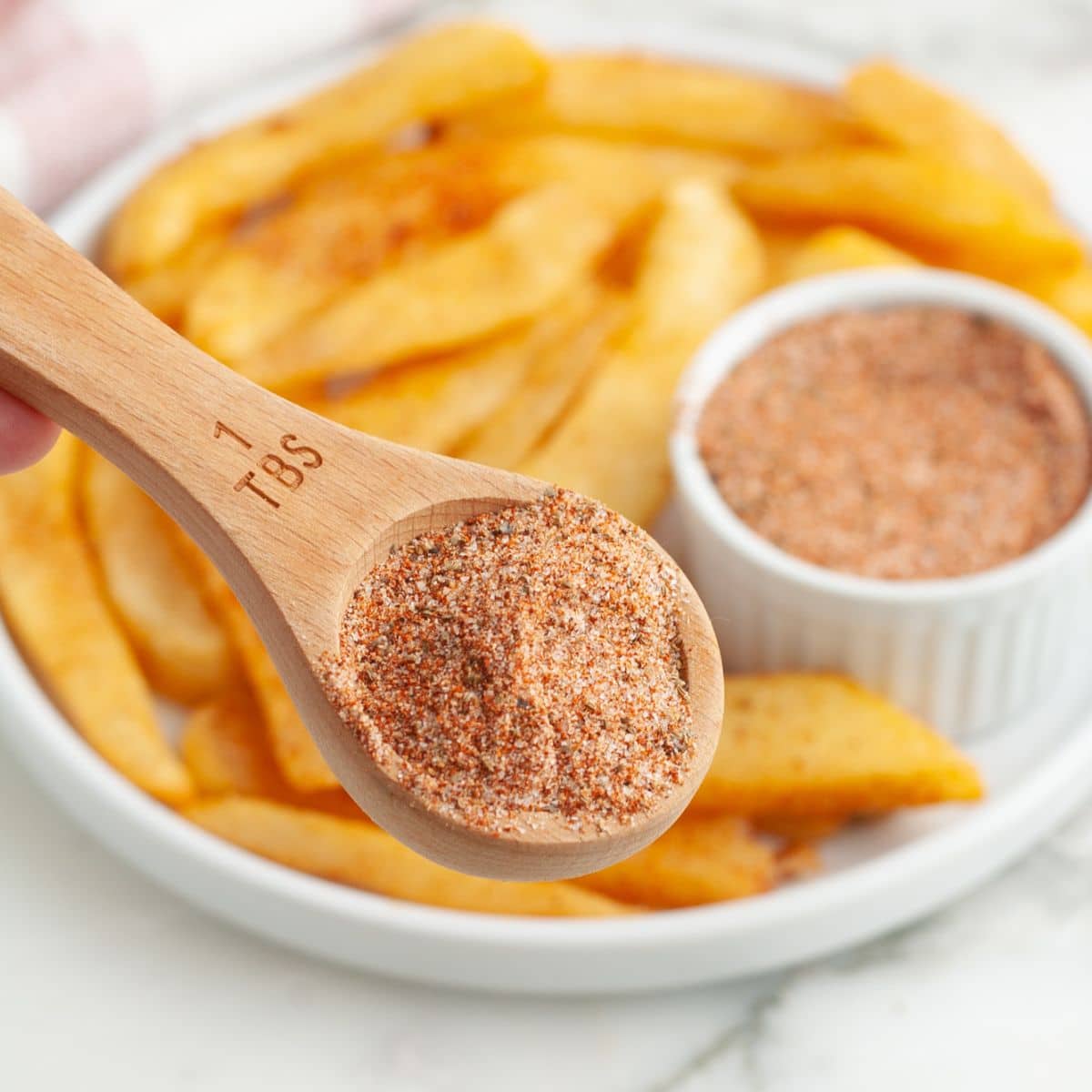 Tablespoon with seasoning and a plate of fries.